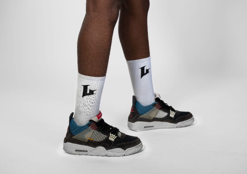 Person wearing black sneakers with colorful design and white socks with a logo on a light gray background