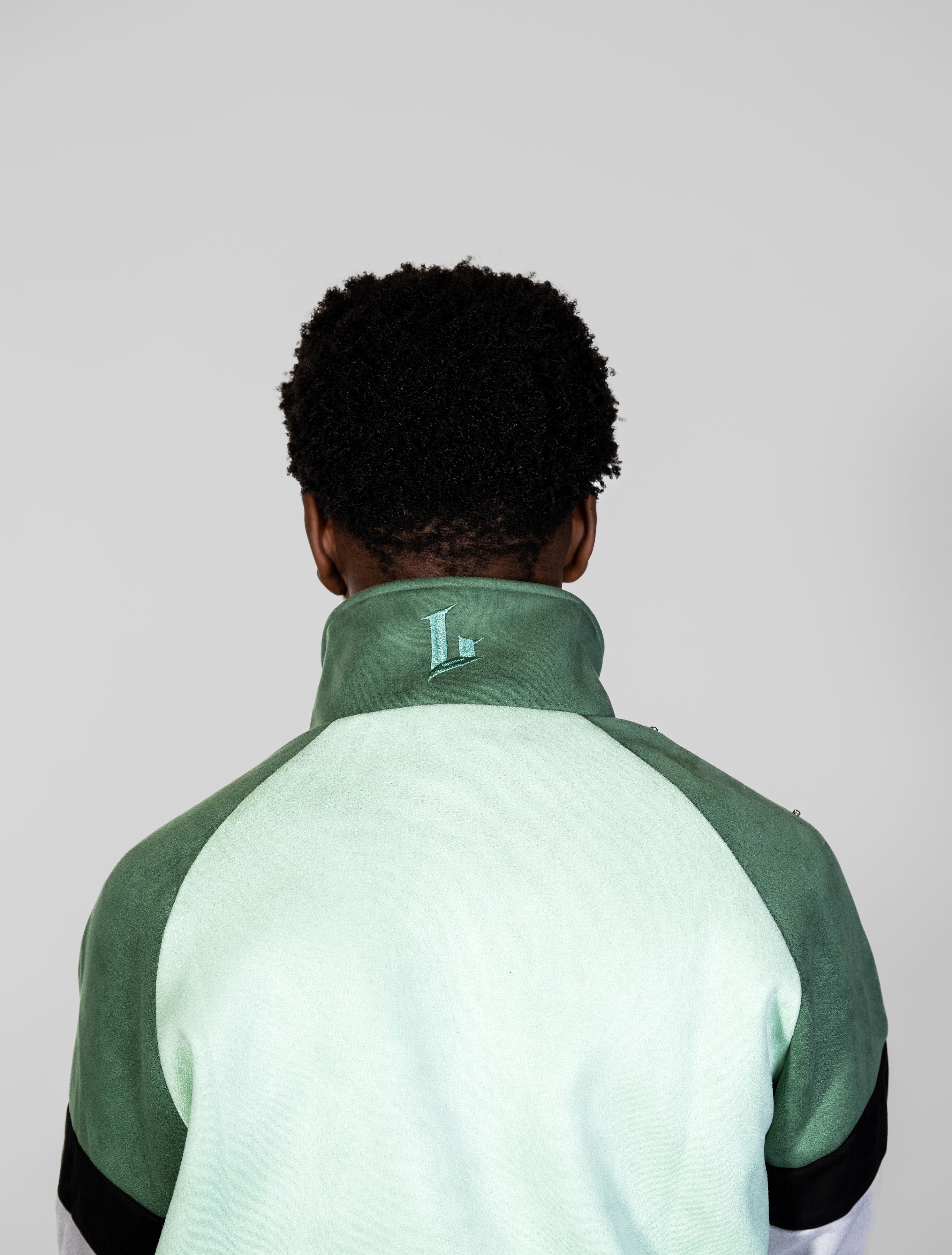 Person wearing a green and light green jacket with a logo on the back against a plain background