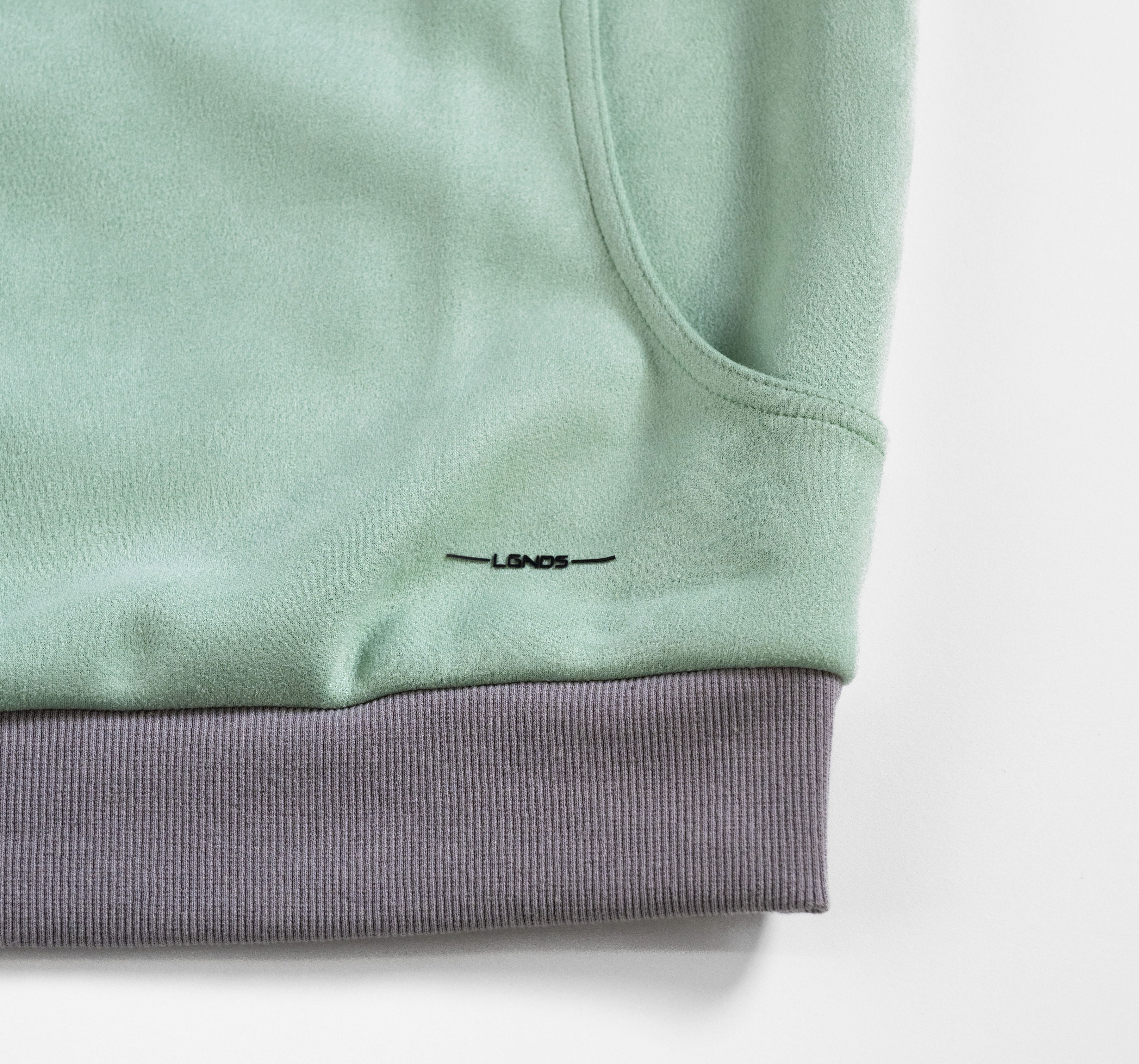 Close-up of a light green sweatshirt with a brand logo on a white background