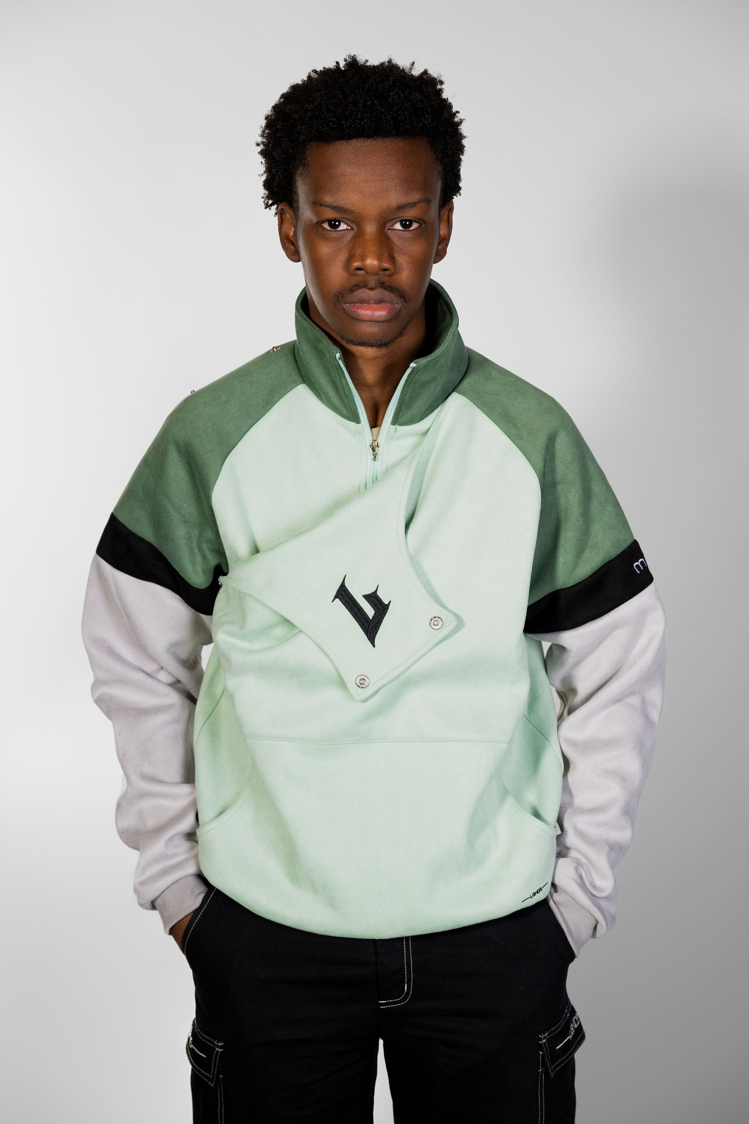 Person wearing a green and gray jacket with a logo on a plain background