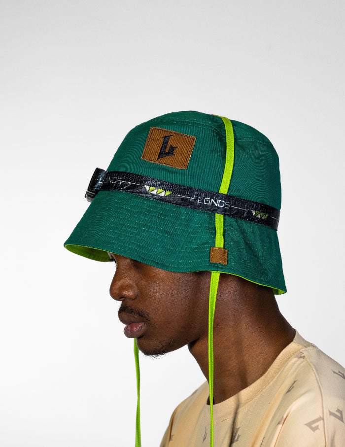 Green bucket hat with a brand logo and strap worn by a person on a white background