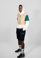 Person wearing a beige and green jacket with a white hoodie on a gray background
