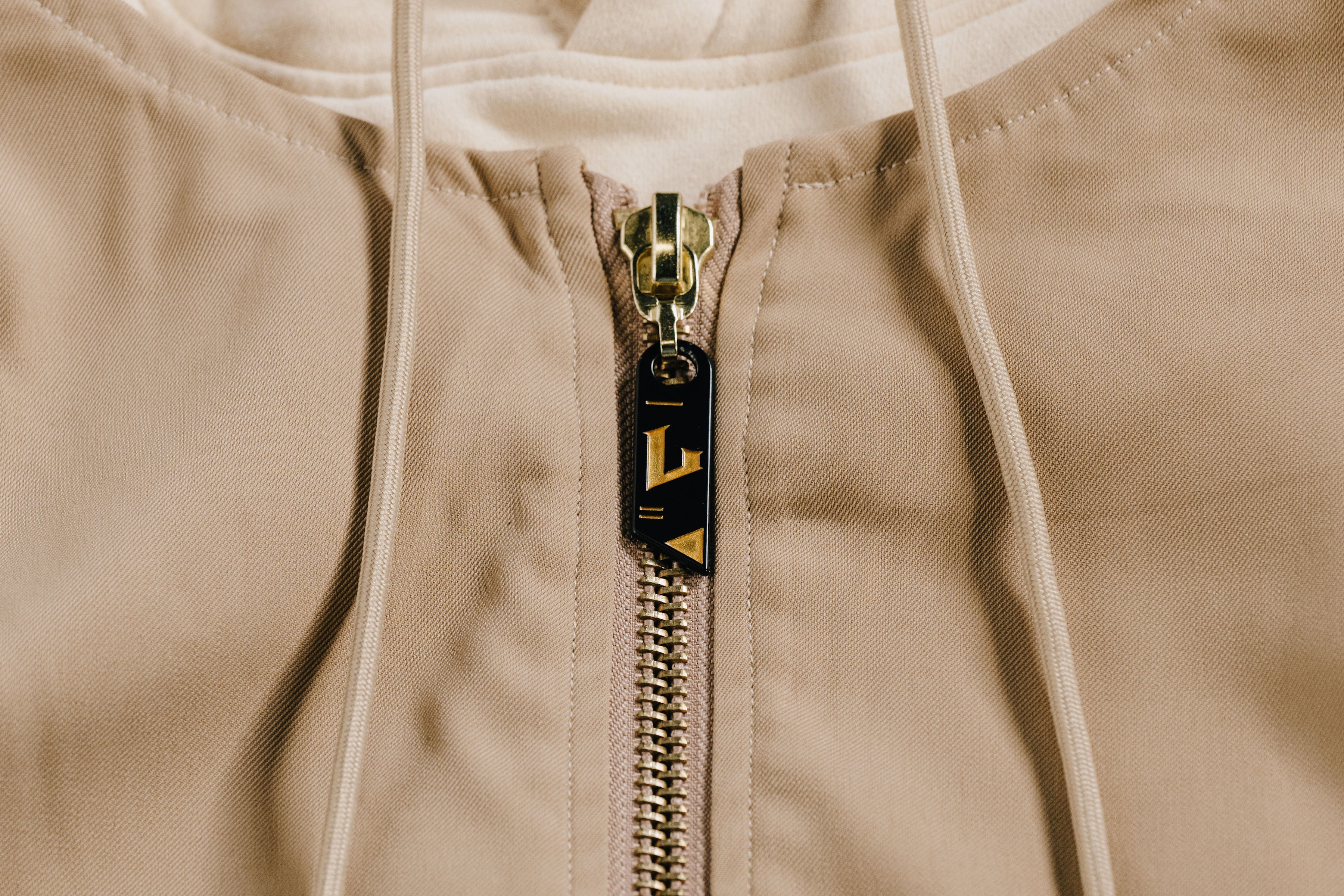 Close-up of a beige jacket with a gold zipper and brand logo.