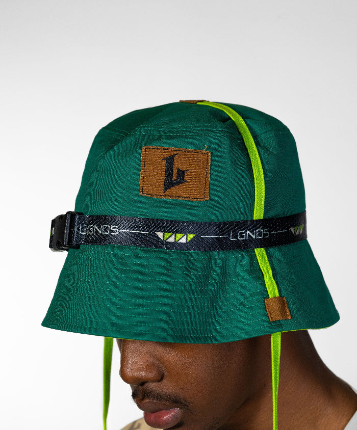 Green bucket hat with a brown patch and black strap worn by a person on a white background
