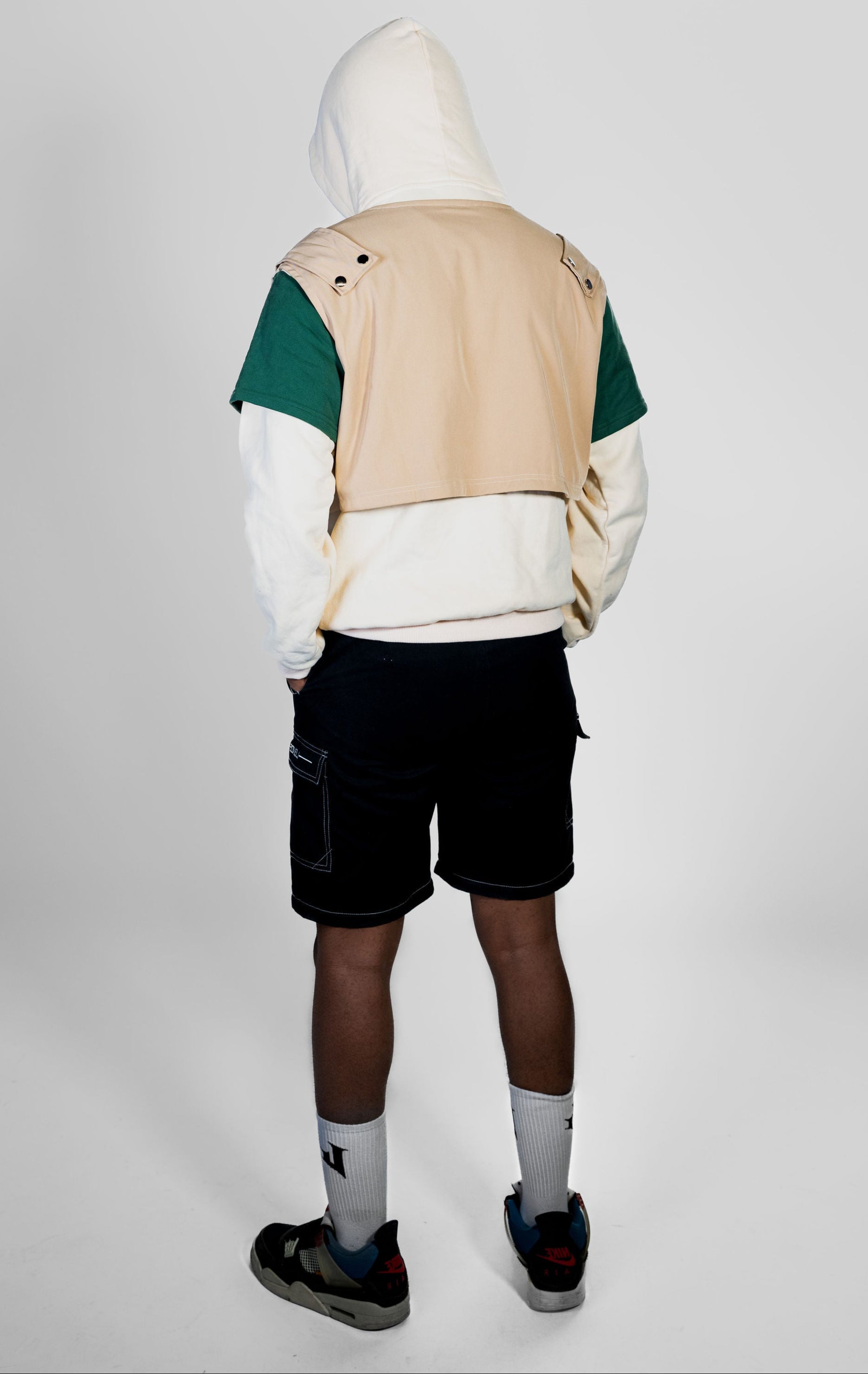 Person wearing a beige and green jacket with a white hoodie on a plain background